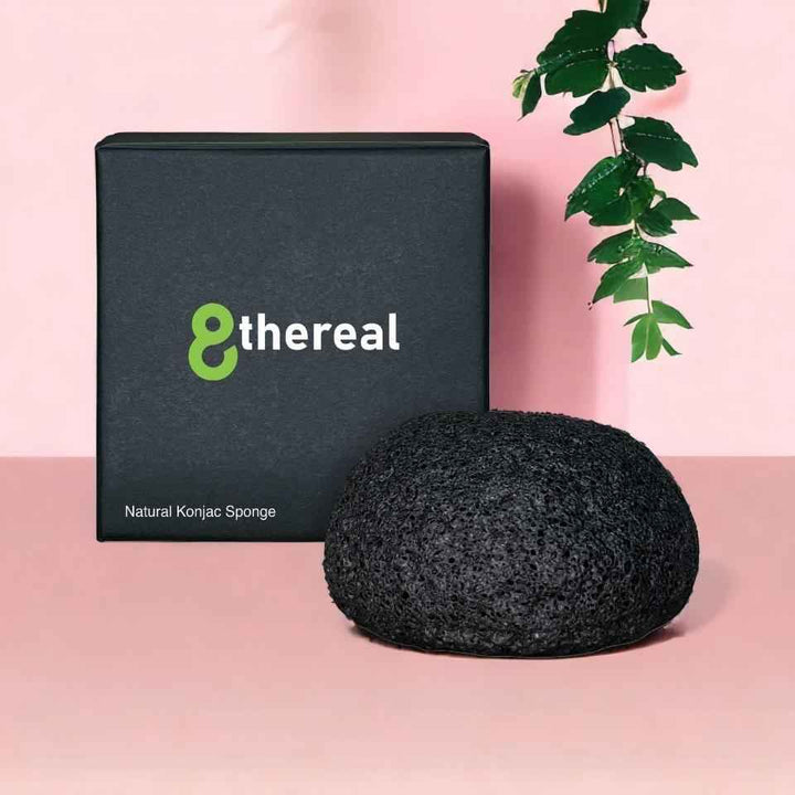 8thereal natural konjac sponge in black, resting in front of its branded black packaging on a soft pink surface.
