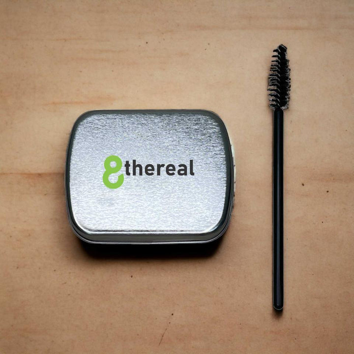 8thereal clear brow soap in a silver metal tin with a black spoolie brush for lifting and shaping eyebrows.