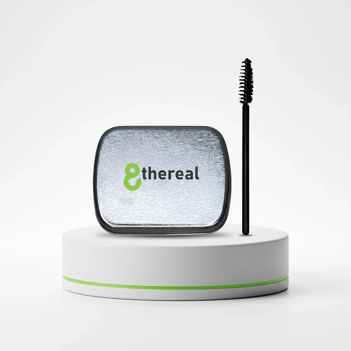 8thereal clear brow soap in a silver metal tin with a black spoolie brush on a white pedestal