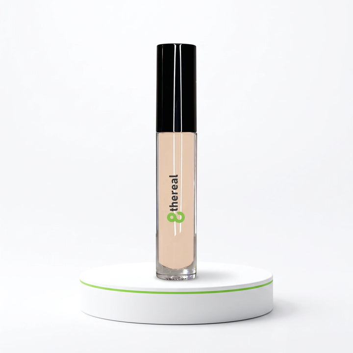 8thereal cream concealer in a clear tube with a black cap, standing on a white circular pedestal against a white background.
