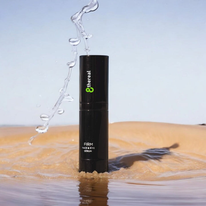 8thereal Firming Face & Eye Serum bottle standing in water with a refreshing splash against a sandy background.