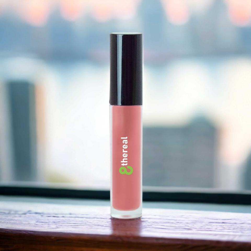 8thereal High-Shine Lip Gloss in a soft pink shade with a clear tube and black cap, standing on a wooden surface.