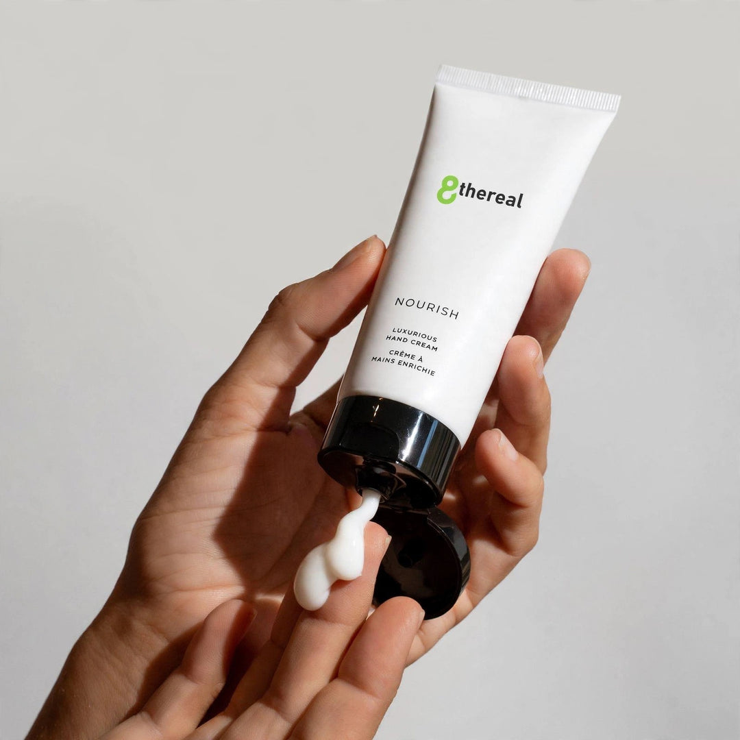 8thereal Restorative Nourish Hand Cream in a white squeeze tube with a dollop of rich white cream on a person's hand.