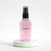 8thereal oil control setting spray in a clear pink bottle with a black pump on a white circular display stand.