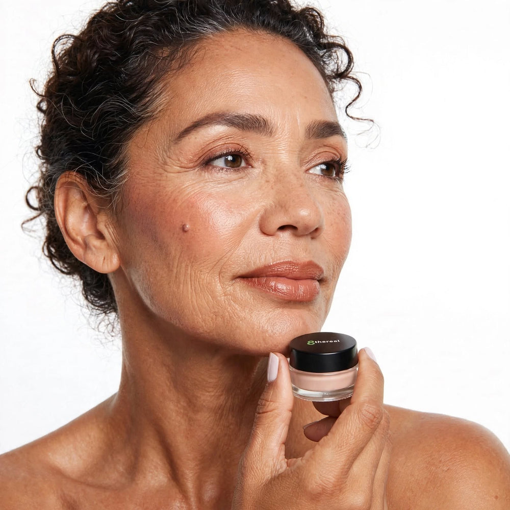8thereal Smoothing Eye & Lip Primer in a small glass jar held by a woman with a natural, radiant makeup look.