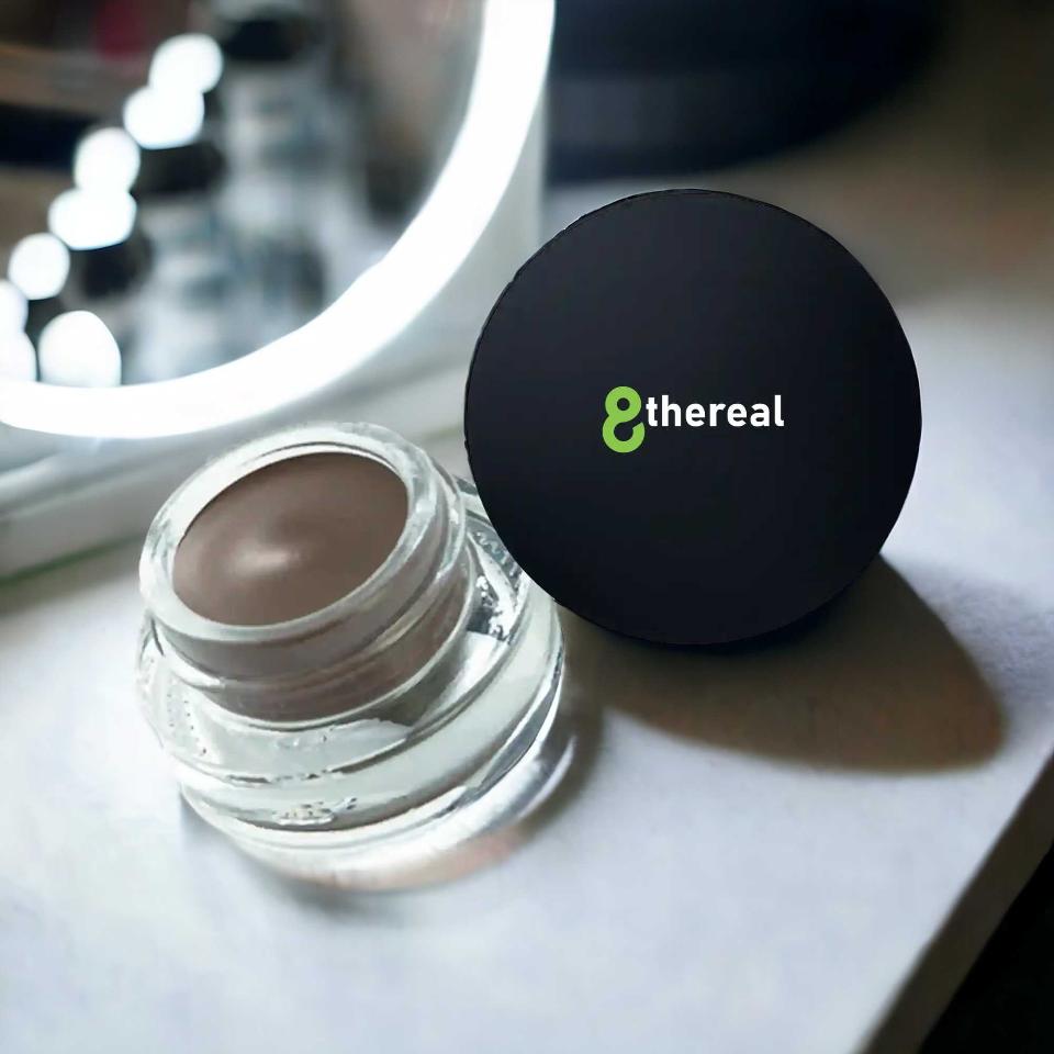 8thereal Soft Sculpt Brow Pomade in a small glass jar with a black lid, featuring a creamy matte brown formula.