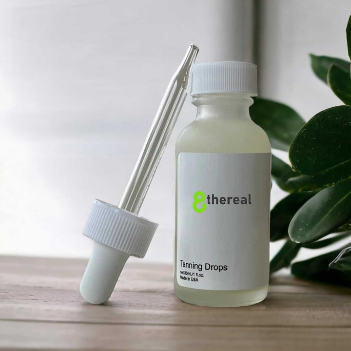 8thereal Sunlit Glow Tanning Drops in a glass bottle with a dropper, set on a wooden surface with green leaves.