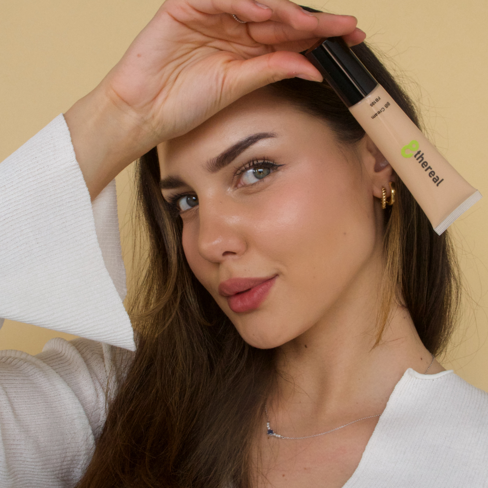 Woman holding a tube of '8thereal' product near her face against a beige background