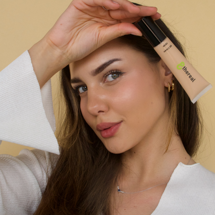 Woman holding a tube of '8thereal' product near her face against a beige background