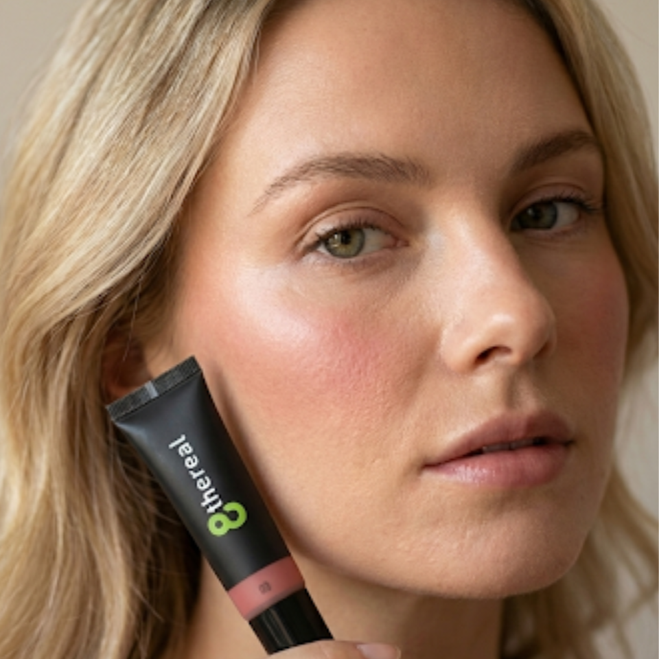 Woman holding a cosmetic tube labeled '8thereal' near her face.